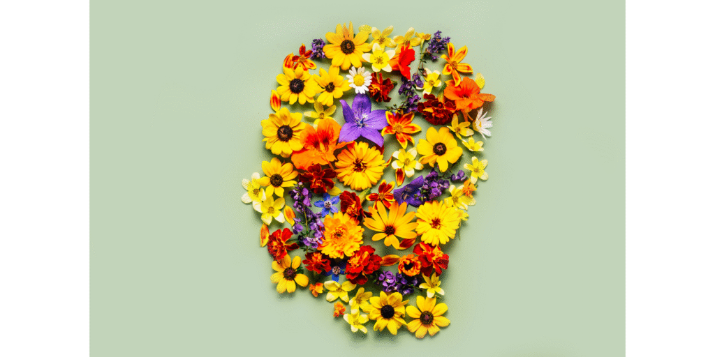 A collection of diverse, colorful flowers arranged perfectly into the shape of a human head profile on a light green background. This artistic visual highlights holistic wellness and nurturing emotional and physical resilience at Port Perry Wellness Centre.