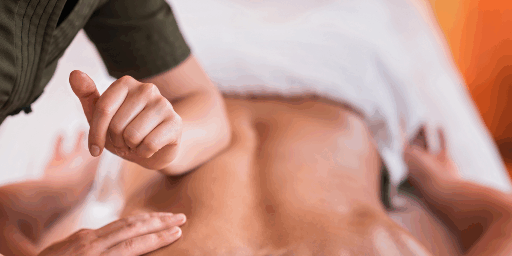 A close-up view of a massage therapist's hand and forearm applying deep pressure to a person’s lower back during a treatment session. Another hand is placed gently on the side for stability.