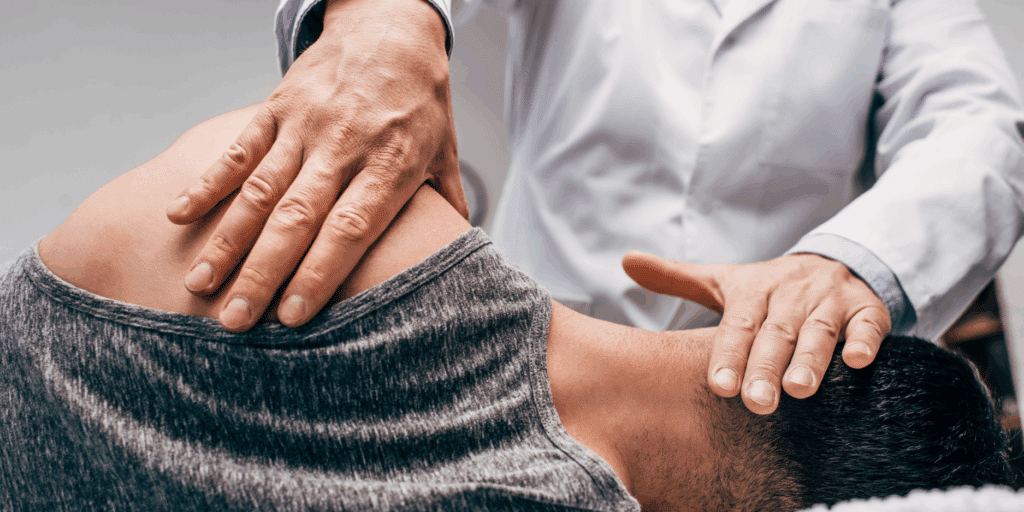 A close-up of a healthcare professional in a white lab coat performing a manual adjustment. One hand is placed on the patient's shoulder and the other is supporting the base of the head/neck while the patient lies face down.