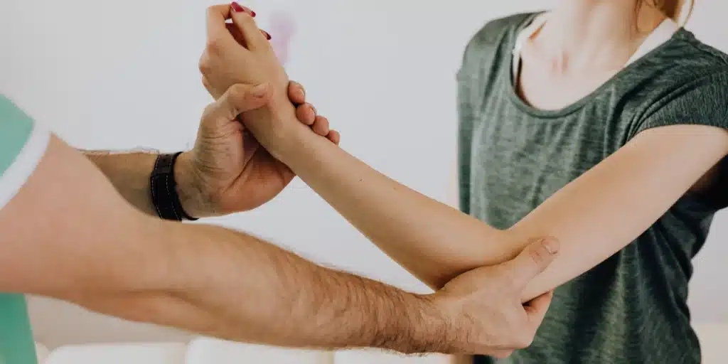 Healthcare professional supporting a person’s forearm and wrist during a physical therapy or mobility assessment.