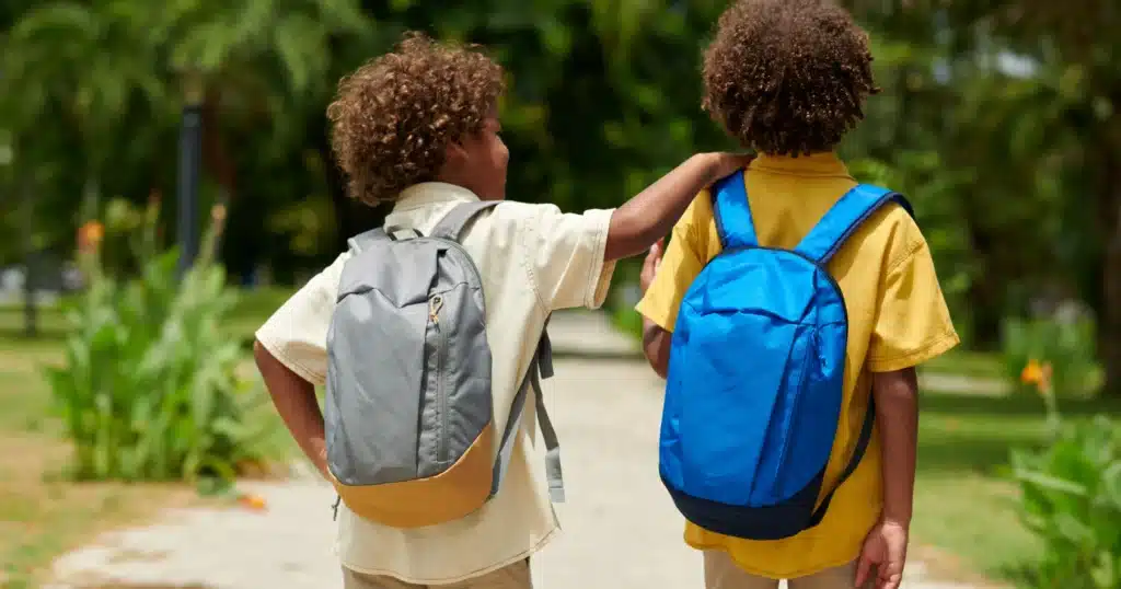 Two young students carrying heavy backpacks on their way to school, showing how posture issues that develop from sitting for long hours at desks can be addressed with chiropractic care and massage therapy services at Port Perry Wellness Centre.