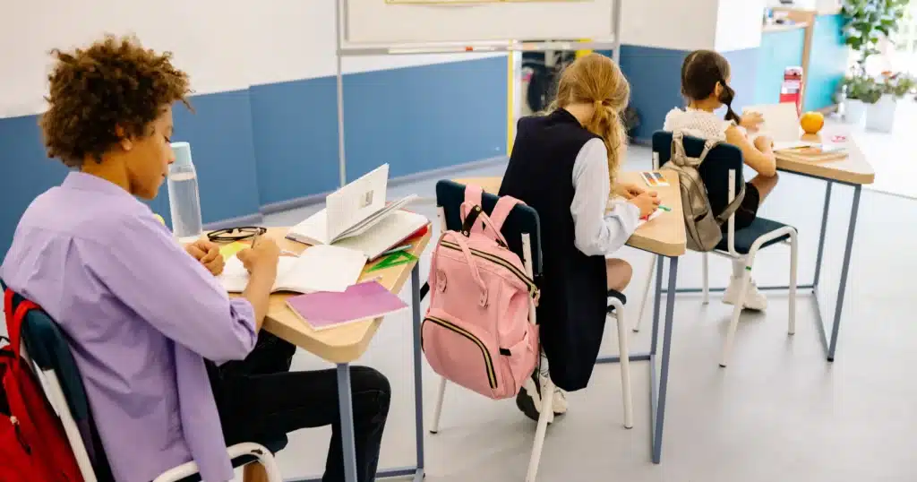 Students sitting at individual desks in a classroom writing in their notebooks, demonstrating the sedentary classroom environment where prolonged sitting can lead to spinal discomfort treated by Port Perry Wellness Centre’s chiropractic and massage therapy care.
